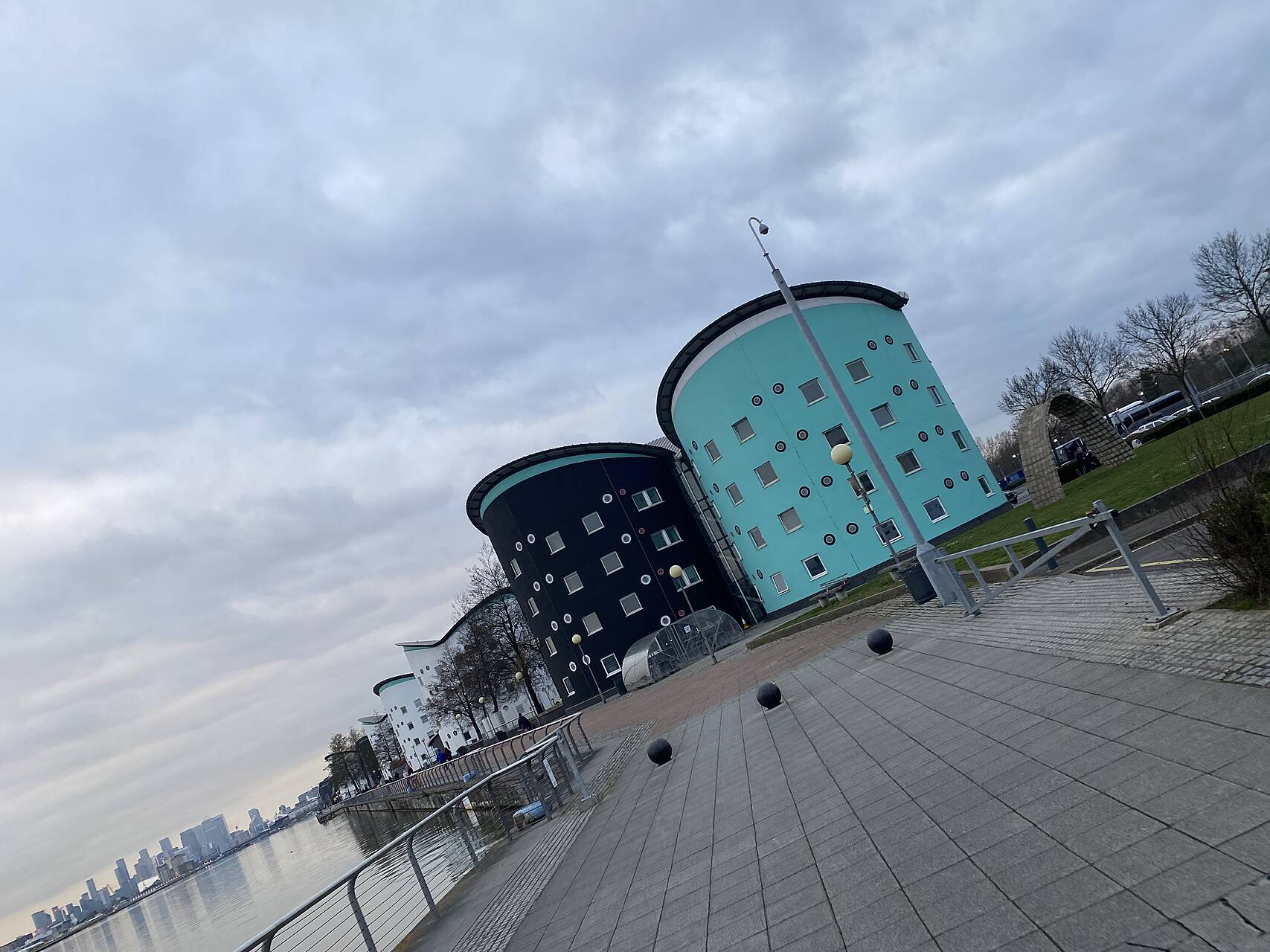Taken from a moving bike, cylindrical residential buildings with colourful walls on a dockside with the London skyline in the background.jpeg